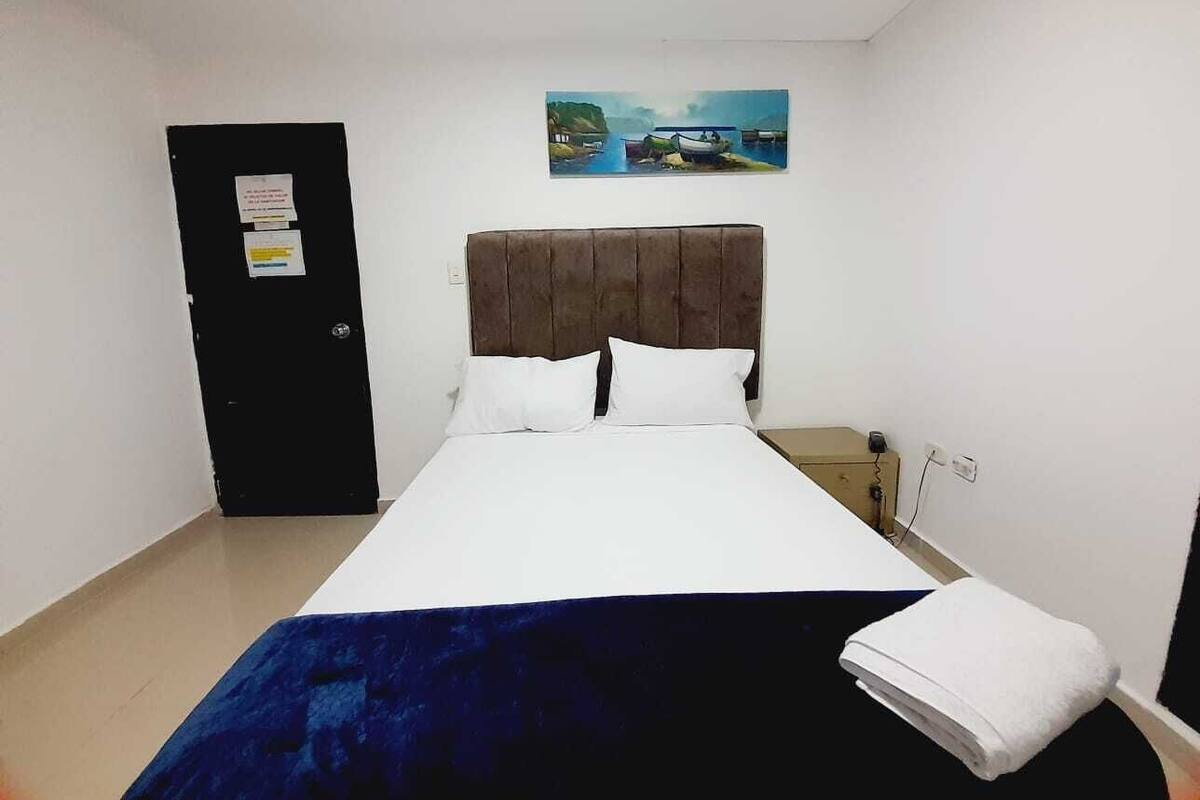 A hotel room with a bed, a nightstand, a wall-mounted painting, a door, and a power outlet.