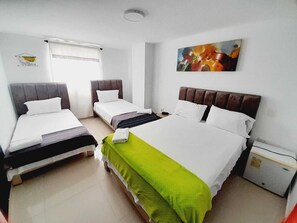 A hotel room with three beds, a small bedside table, and a wall-mounted painting. - Hotel Karin (Riohacha)