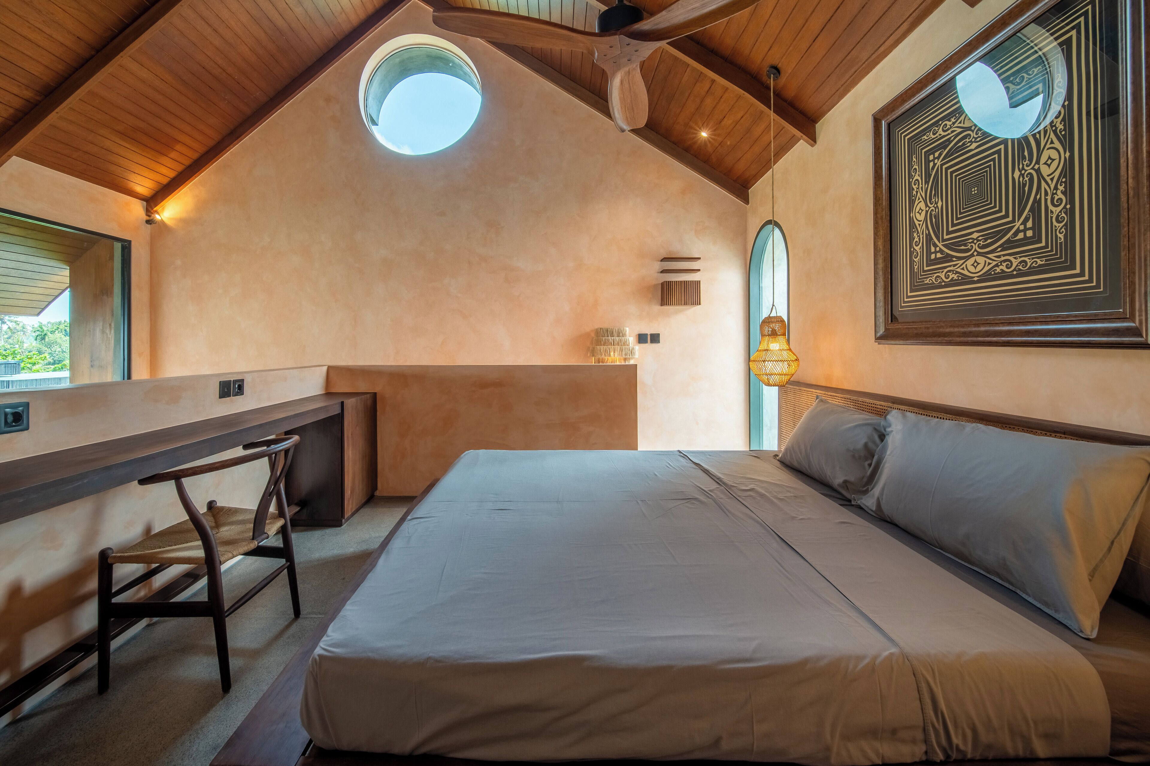 A bedroom with a bed, a desk, and a chair. There is a window and a ceiling fan.