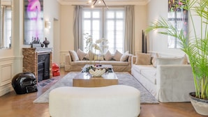 A spacious living room with a modern fireplace, a large window with curtains, a comfortable sofa set, and a central coffee table. - Luxury Mansion With Garden in Heart of Neuilly (Neuilly-sur-Seine)