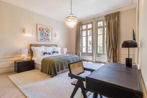 Una camera da letto con un letto, comodini, una scrivania, una sedia, un lampadario e una finestra con tende.