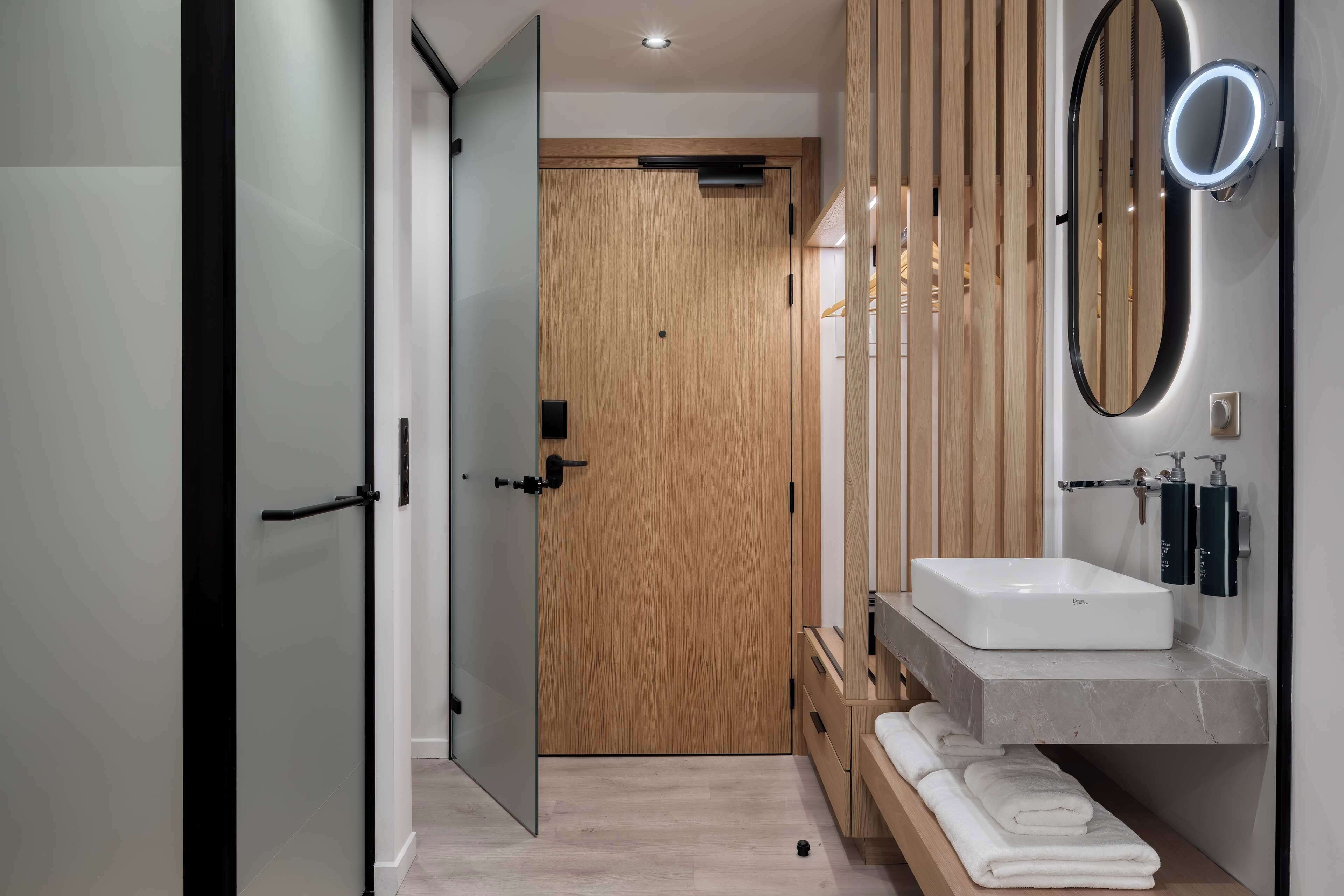 Un baño moderno con puerta de madera, un lavabo blanco y un espejo con luz.