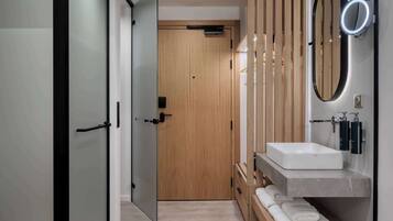 Un baño moderno con puerta de madera, un lavabo blanco y un espejo con luz.