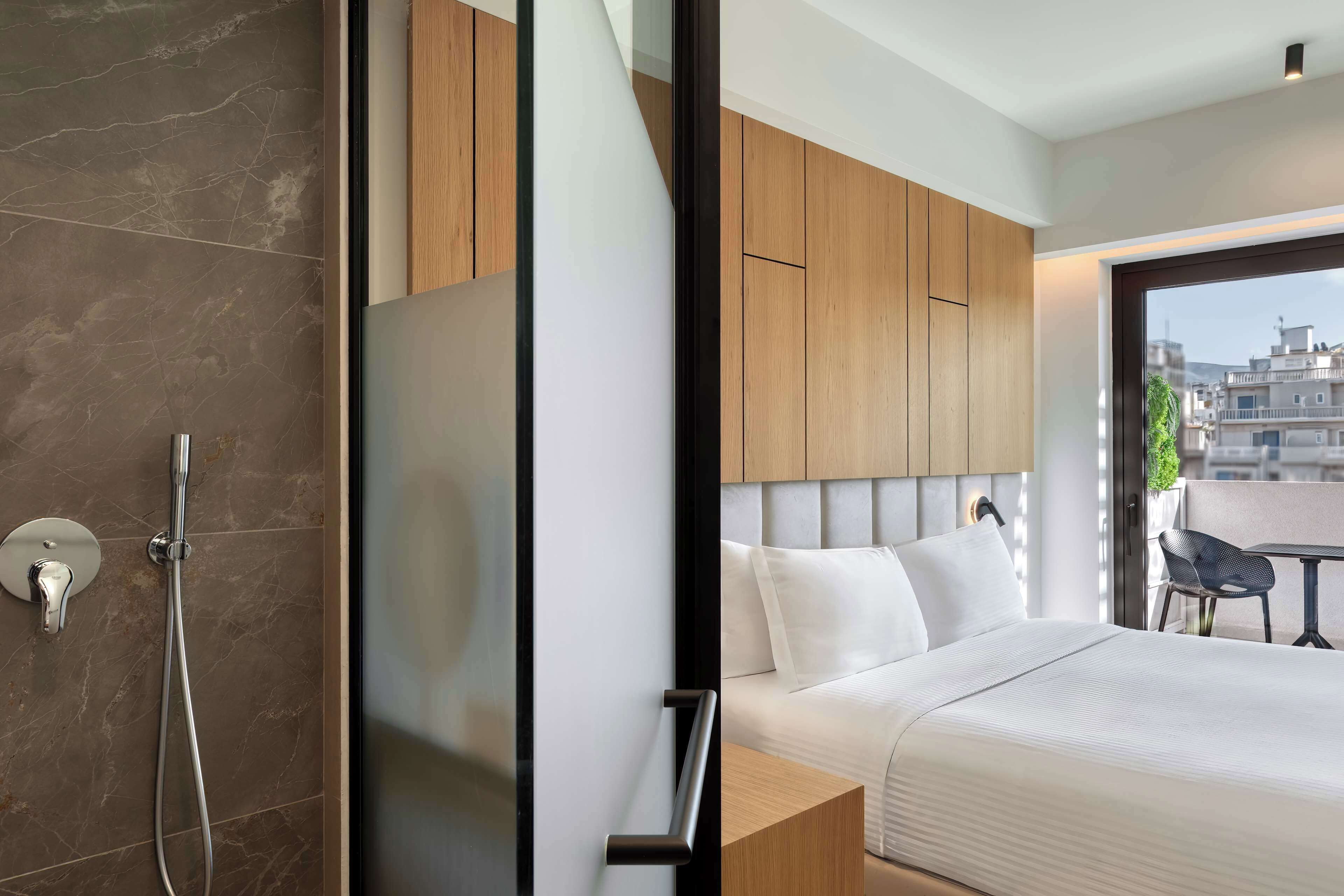 Een moderne hotelkamer met een groot bed, een douchegedeelte en stadszicht door een groot raam.