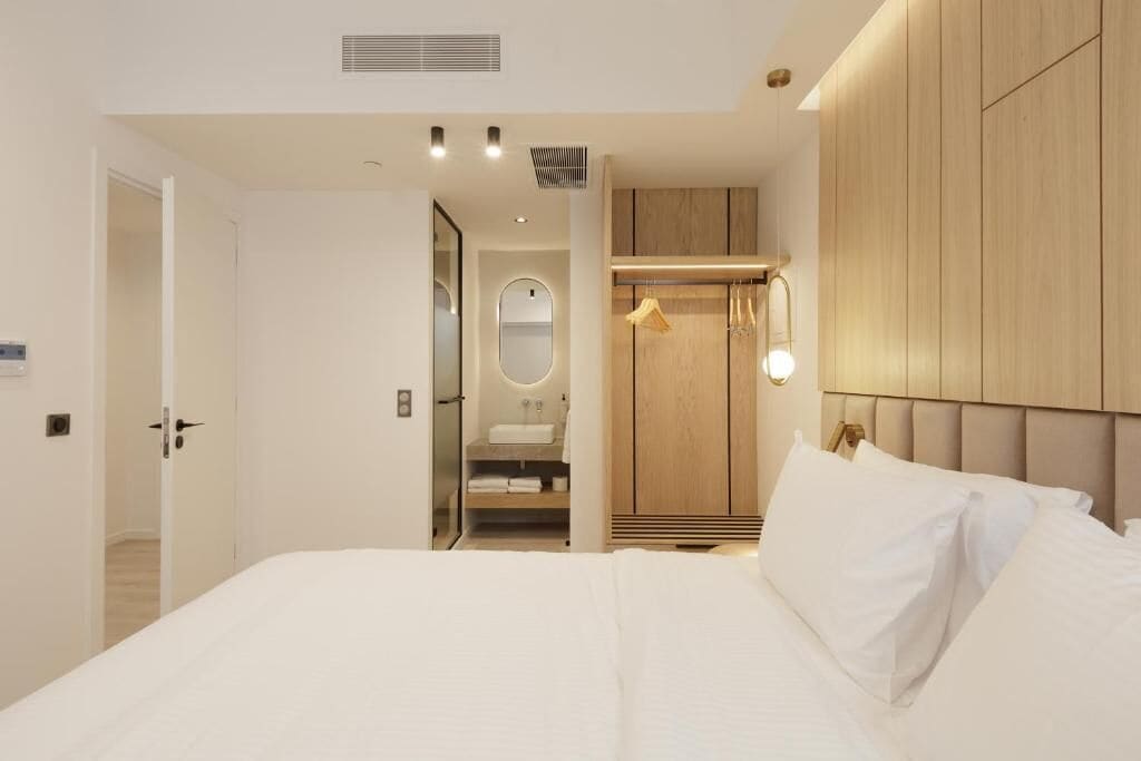A modern hotel room with a large bed, a walk-in closet, and a bathroom with a mirror and sink.