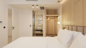 A modern hotel room with a large bed, a walk-in closet, and a bathroom with a mirror and sink.