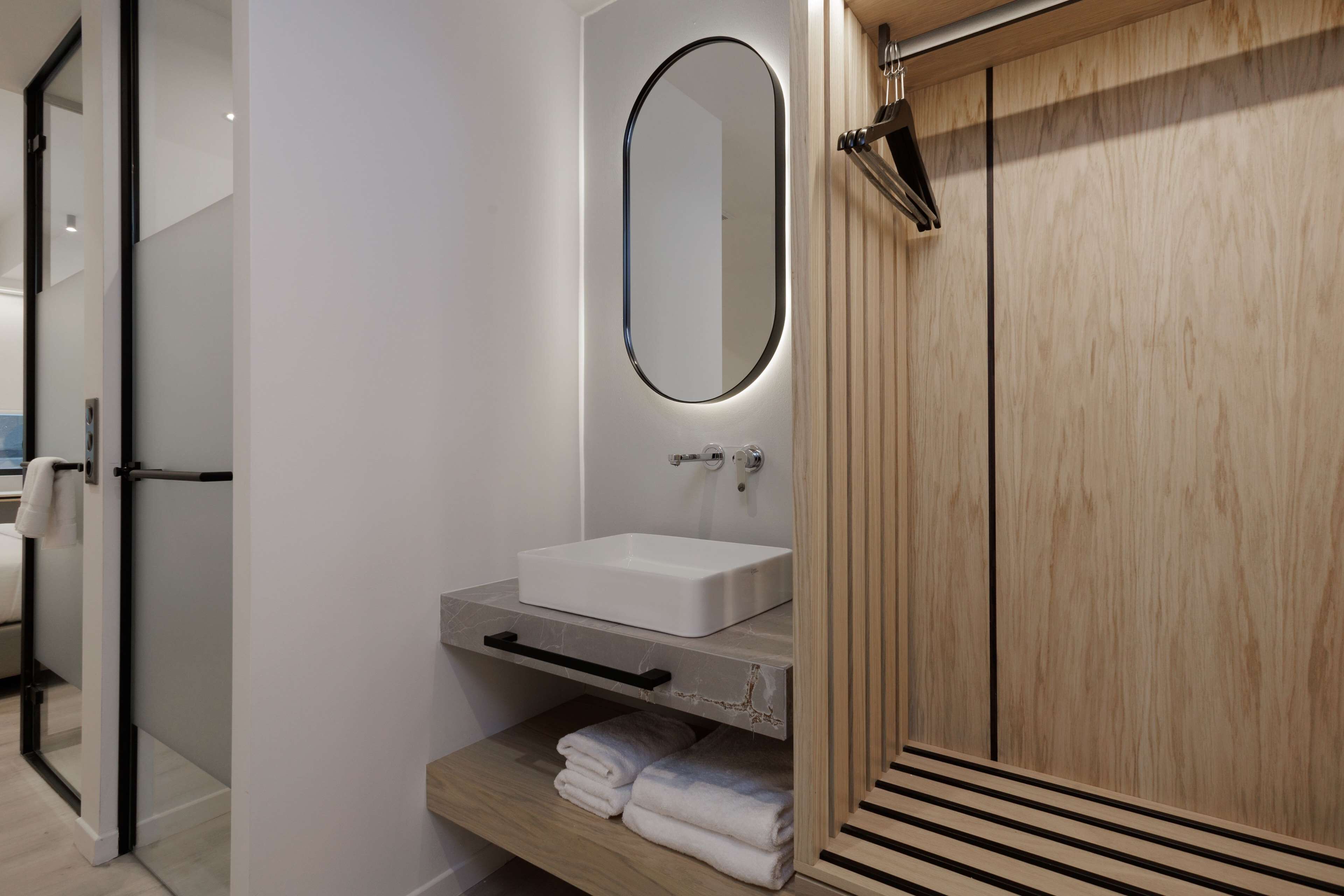 A modern bathroom with a white sink, a mirror, and a wooden wardrobe.
