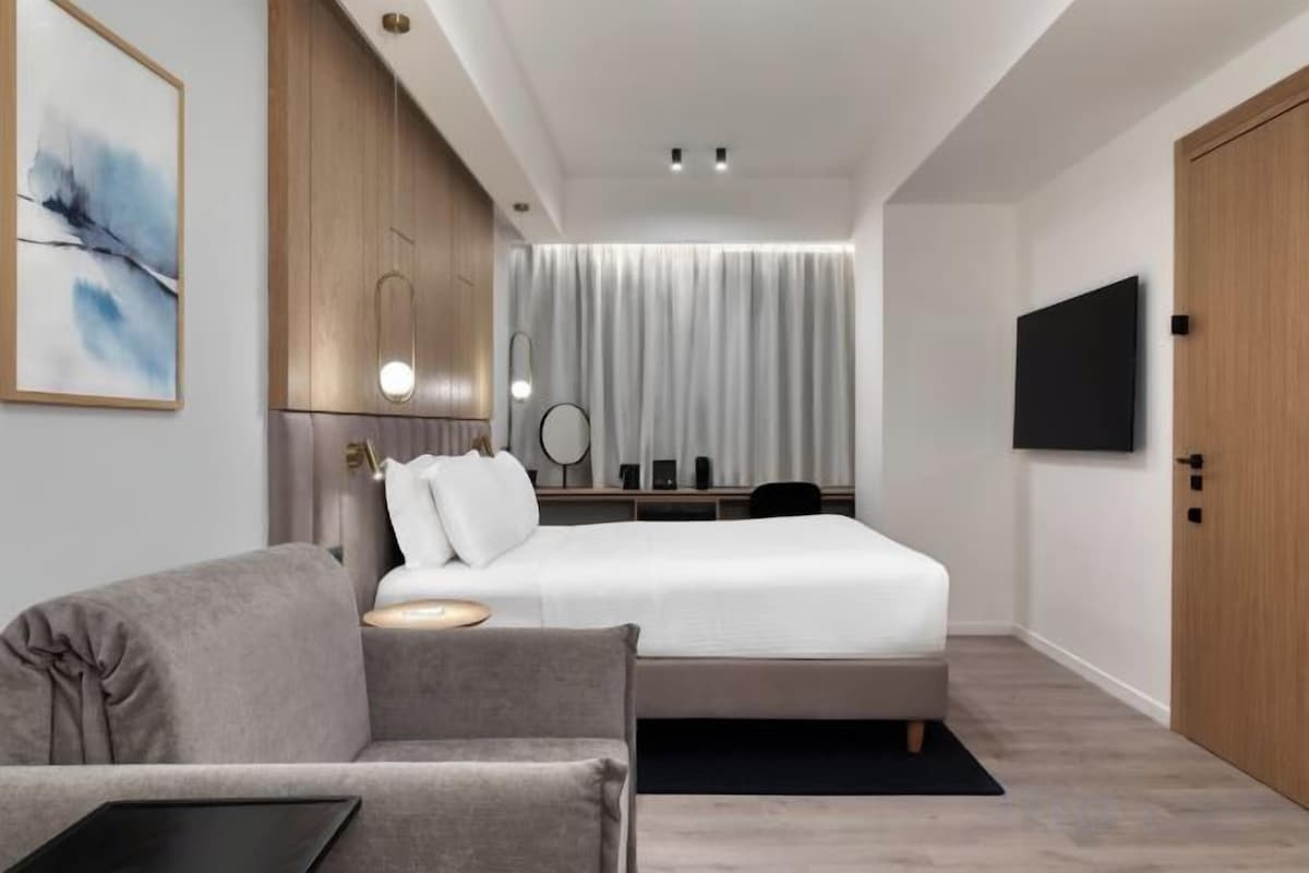A modern hotel room with a bed, a sofa, a flat-screen TV, and a painting on the wall.