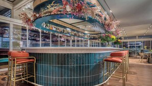 A bar area with a curved counter, multiple shelves with bottles, and bar stools. - Hilton Garden Inn Athens Syggrou Avenue (Kallithea)
