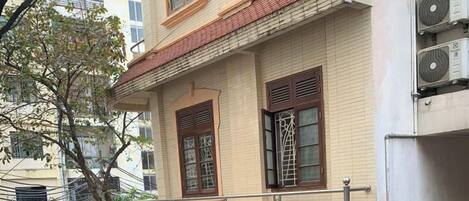 Un edificio residencial de varios pisos con un balcón, una planta en maceta y un coche estacionado en la calle.