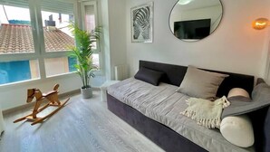 A modern bedroom with a grey sofa, a round mirror, a potted plant, and a rocking horse.