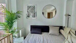 A bedroom with a bed, a round mirror, a zebra print artwork, and a potted plant.