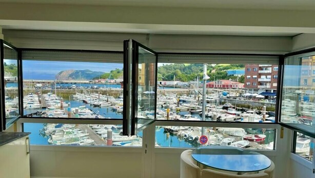 A balcony with a glass railing overlooking a marina with boats and buildings. - Kai begi, wonderful views of the port. (Bermeo)