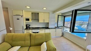 A modern apartment with a green sofa, a kitchen with white cabinets, and a large window offering a view of a marina. - Kai begi, wonderful views of the port. (Bermeo)