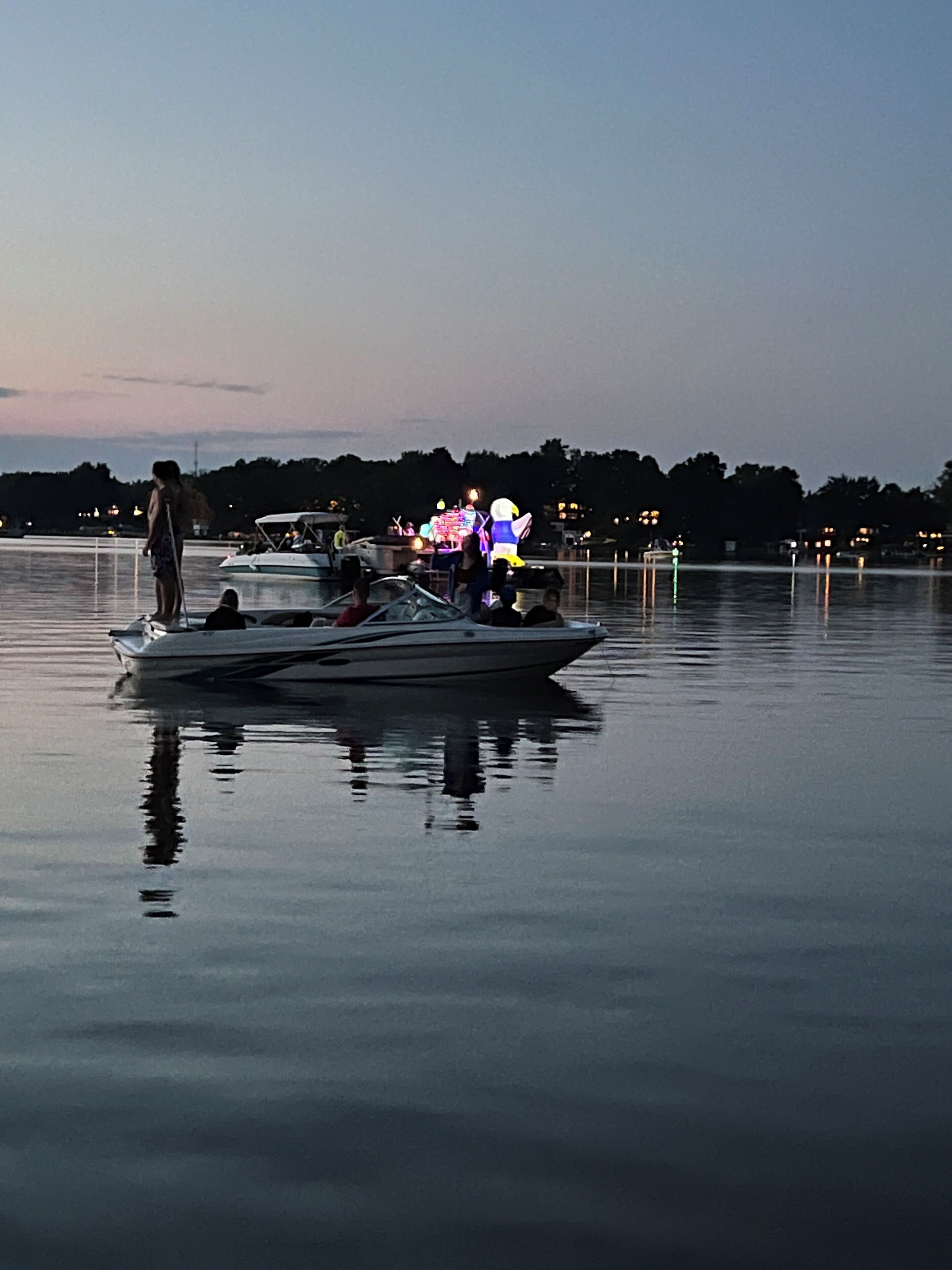Un bote amarrado en un lago tranquilo con un speedboat amarrado y una persona de pie en el muelle.