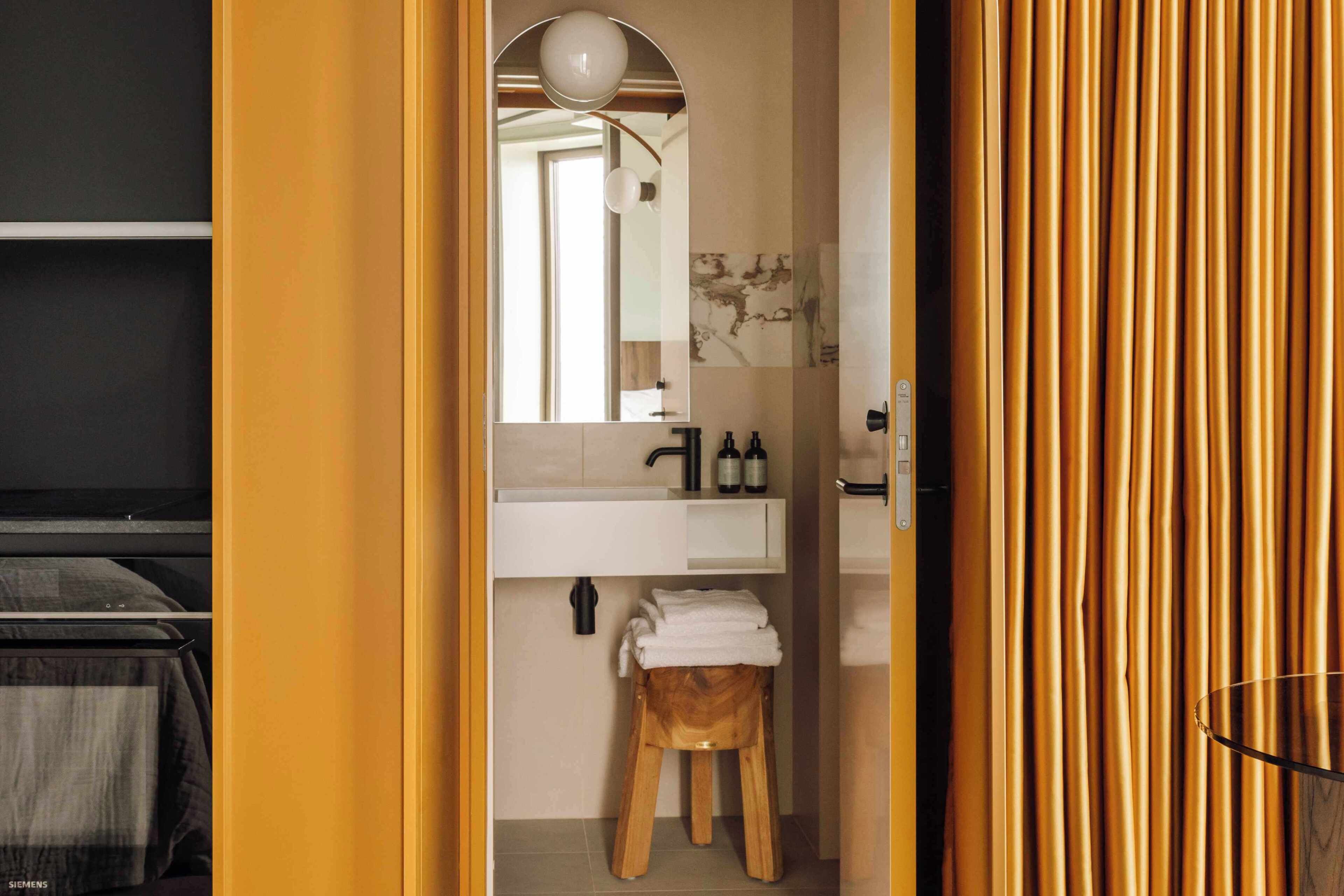 A bathroom with a white sink, mirror, and wooden stool.