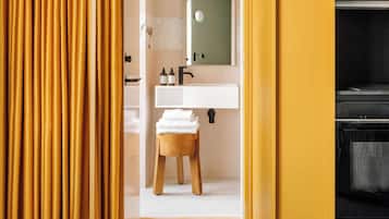 Un baño con un lavamanos blanco, un taburete de madera con toallas y un espejo sobre el lavamanos.