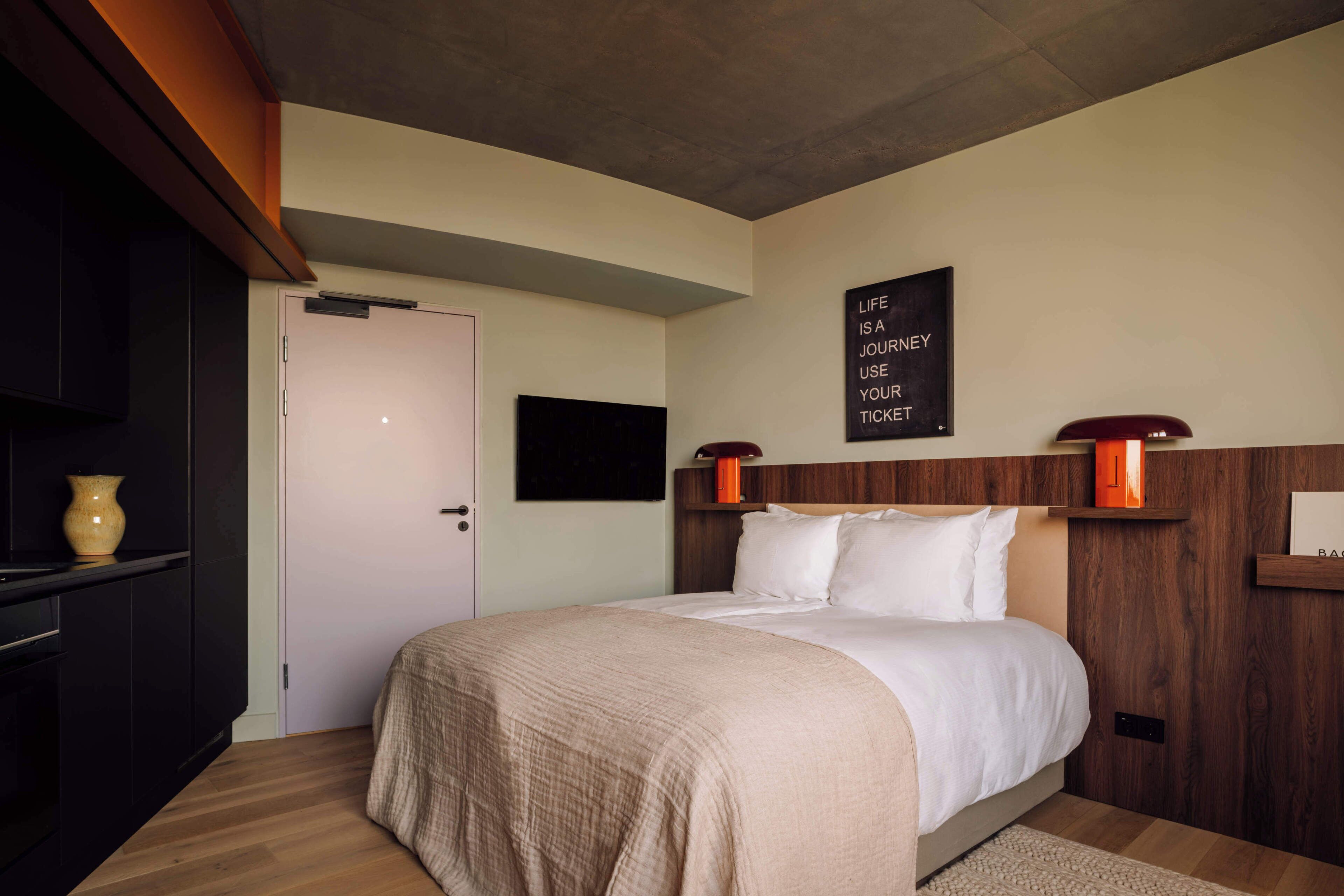 A bedroom with a bed, a wall-mounted TV, a door, and a motivational quote on the wall.