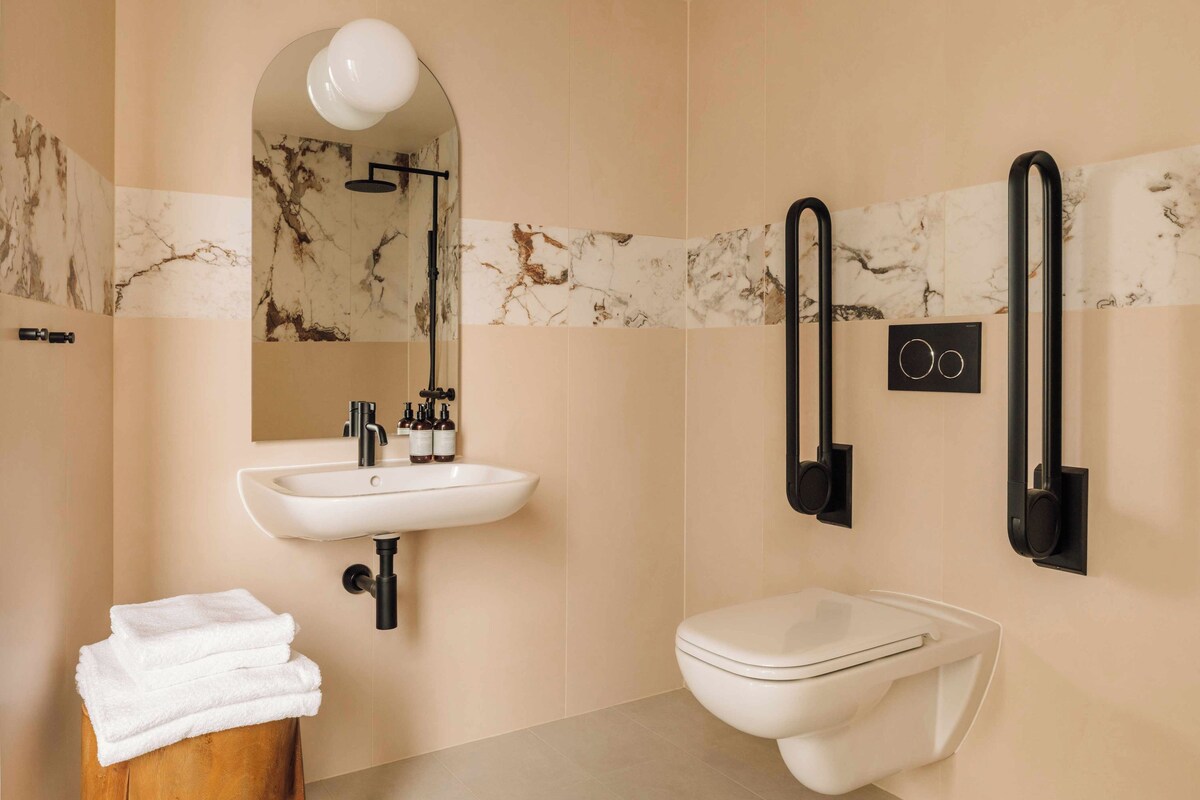 A bathroom with a sink, mirror, toilet, and towel stack.