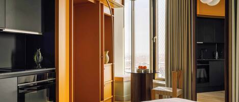 A modern hotel room with a bed, a TV, a wardrobe, and a view of the city.