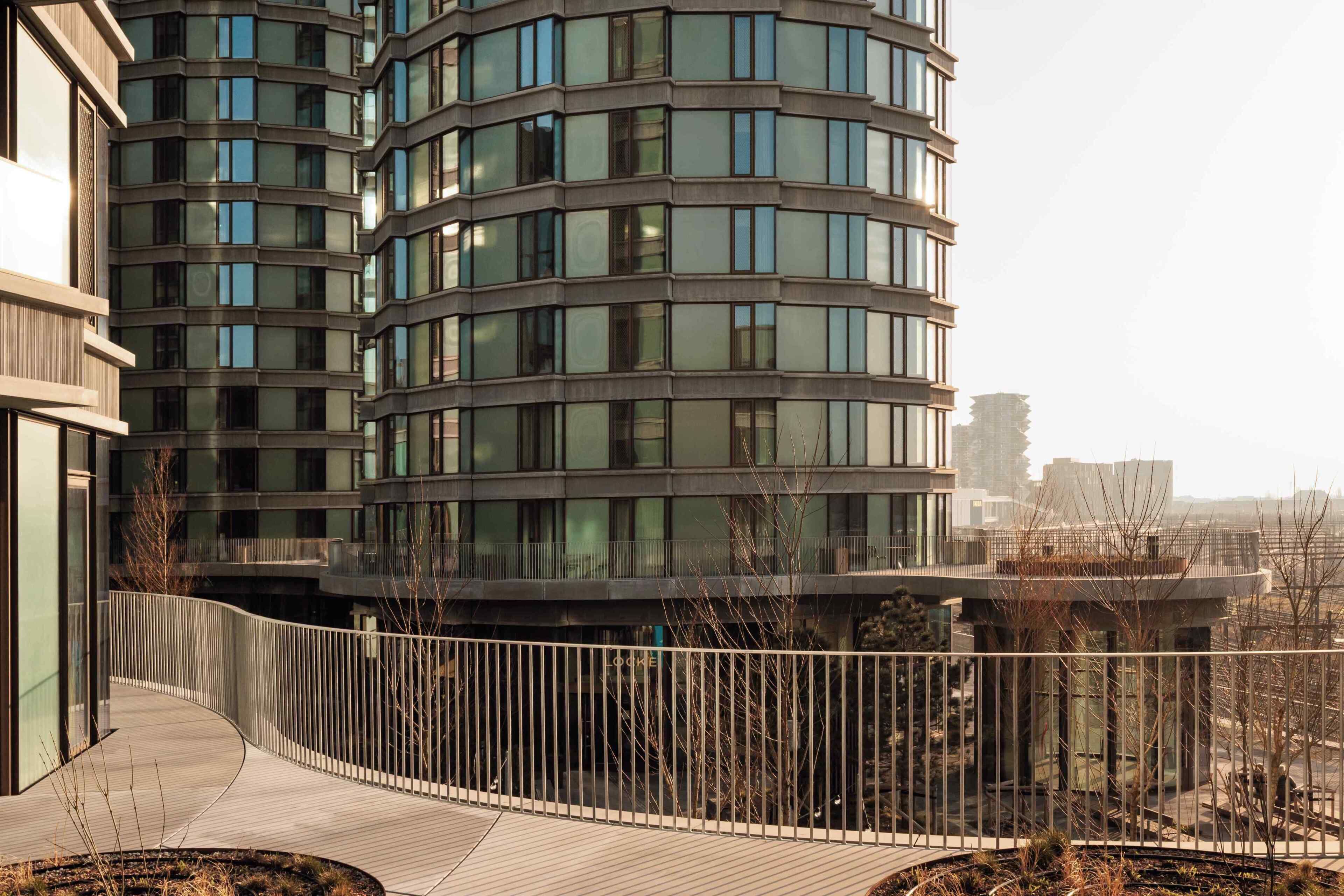 Un edificio moderno con fachada curva, múltiples ventanas y un paseo peatonal.