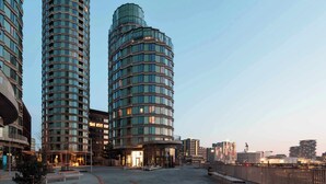 A modern high-rise building with a curved facade, a spacious plaza with benches, and a clear sky.