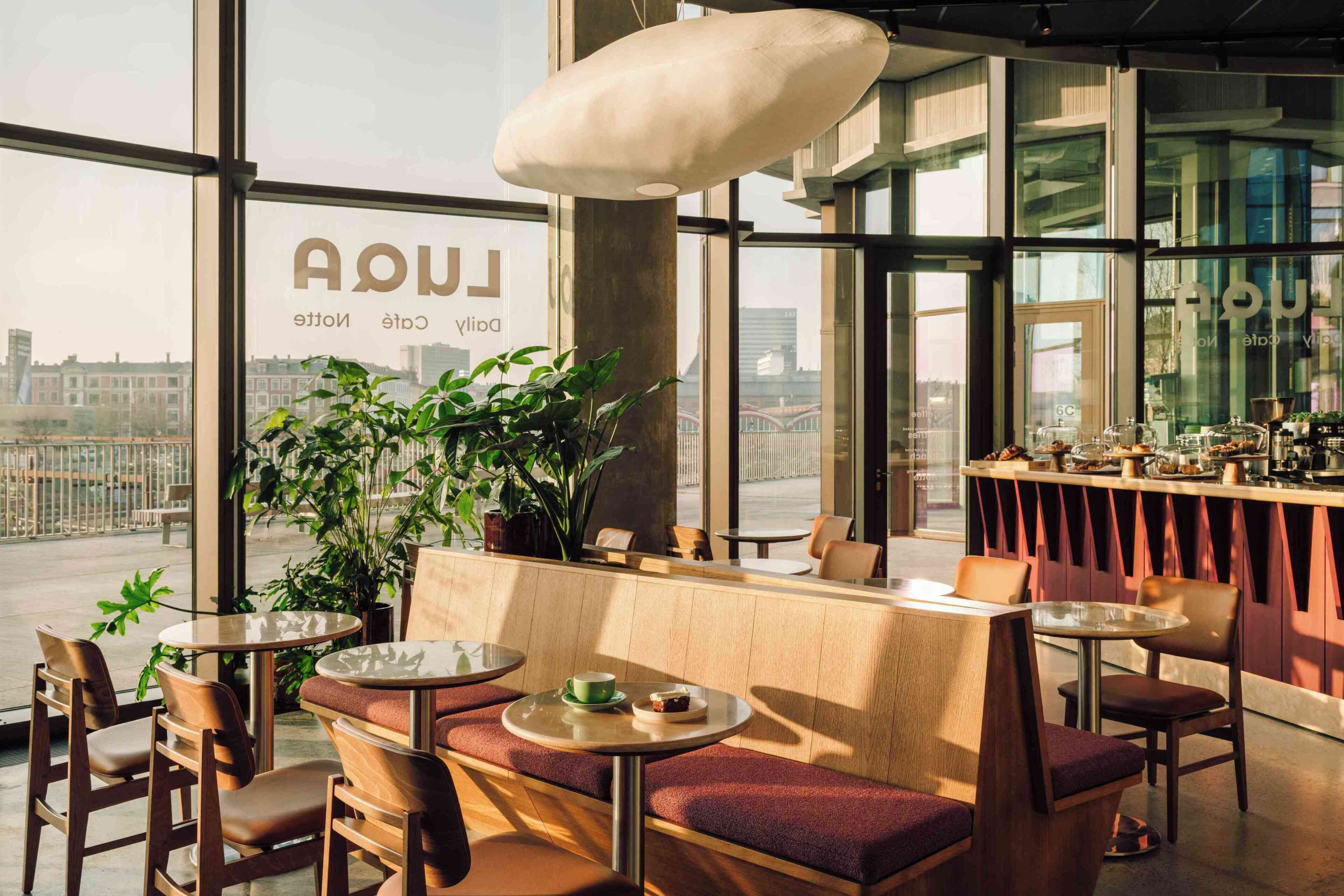 A modern cafe with large windows, seating arrangements, and a bar area.
