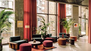 A modern lobby with large windows, red curtains, and various seating arrangements including sofas and ottomans.