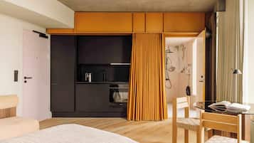 A modern hotel room with a bed, a desk with a chair, a wardrobe, and a bathroom visible through an open door.