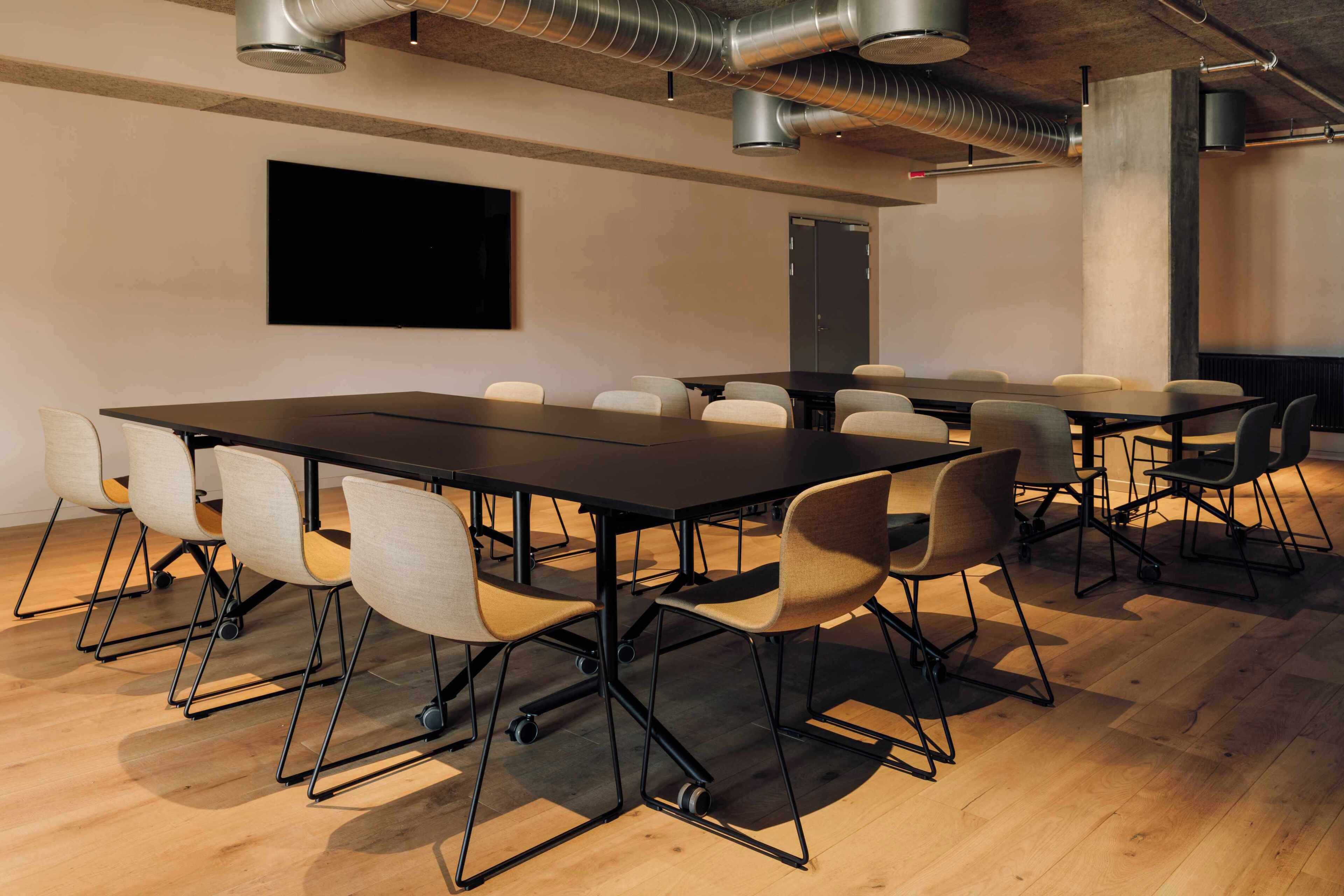 A conference room with a long table, multiple chairs, a mounted screen, and exposed ductwork.