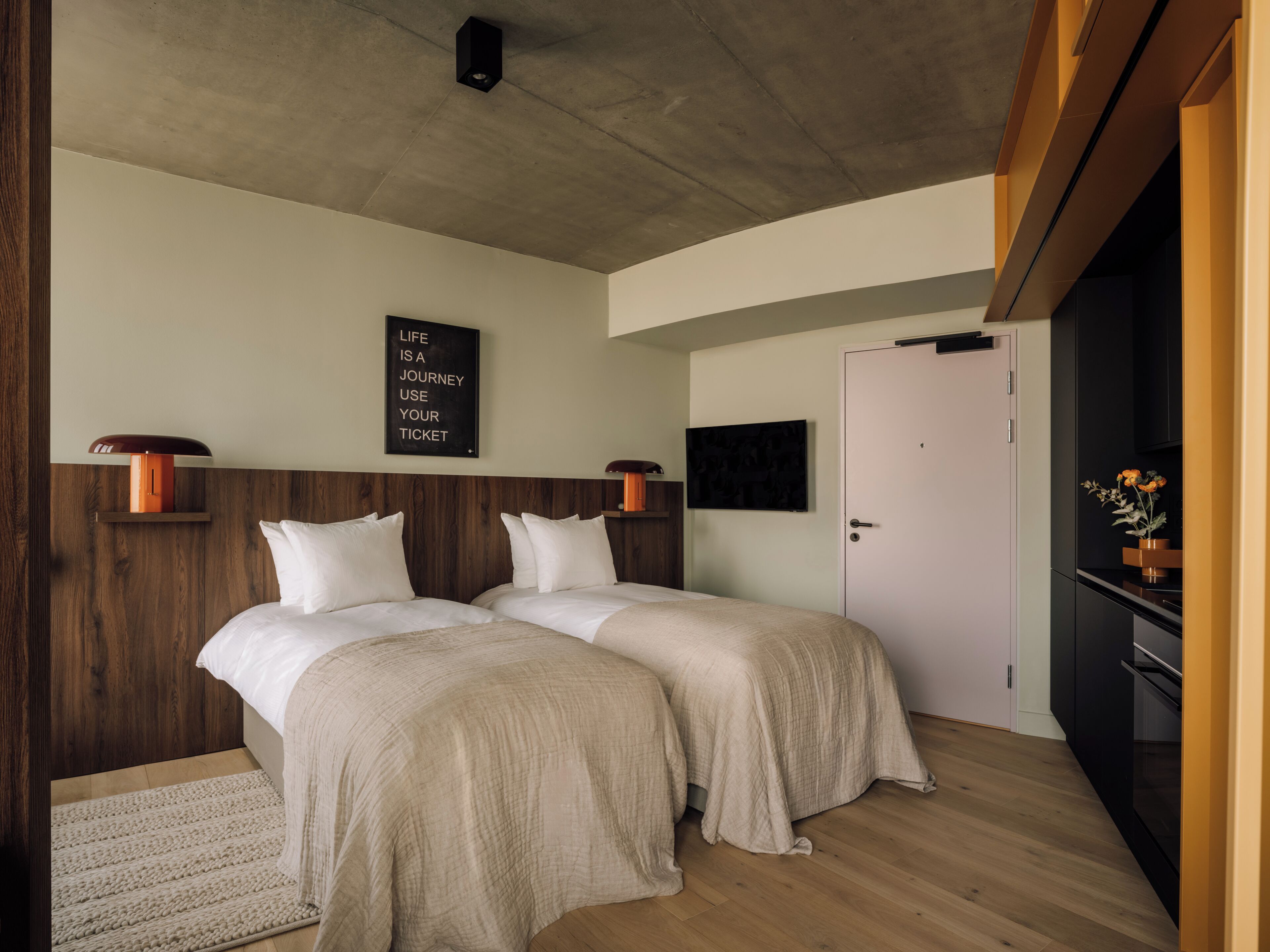 Ein Schlafzimmer mit zwei Betten, einem Holz-Kopfteil, einem an der Wand montierten Fernseher und einer Tür.