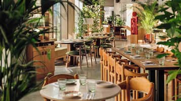 Ein Restaurant mit mehreren Tischen, Stühlen, Zimmerpflanzen und einem modernen Interieur.
