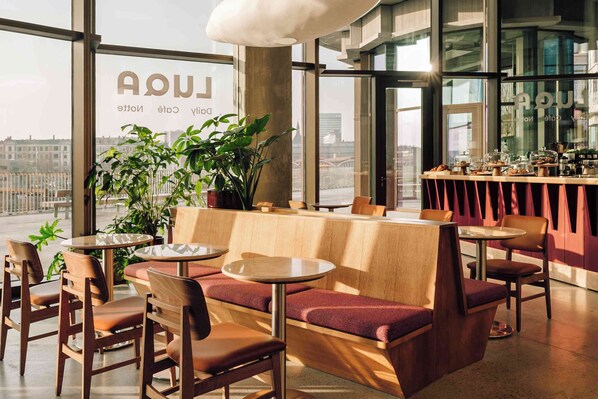 A modern cafe with wooden furniture, a bar area, and large windows offering a city view. - Locke Copenhagen (Copenhagen)