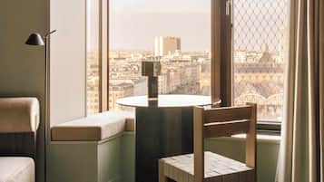 A corner room with a round table and a chair, a sofa, and a large window with a city view.