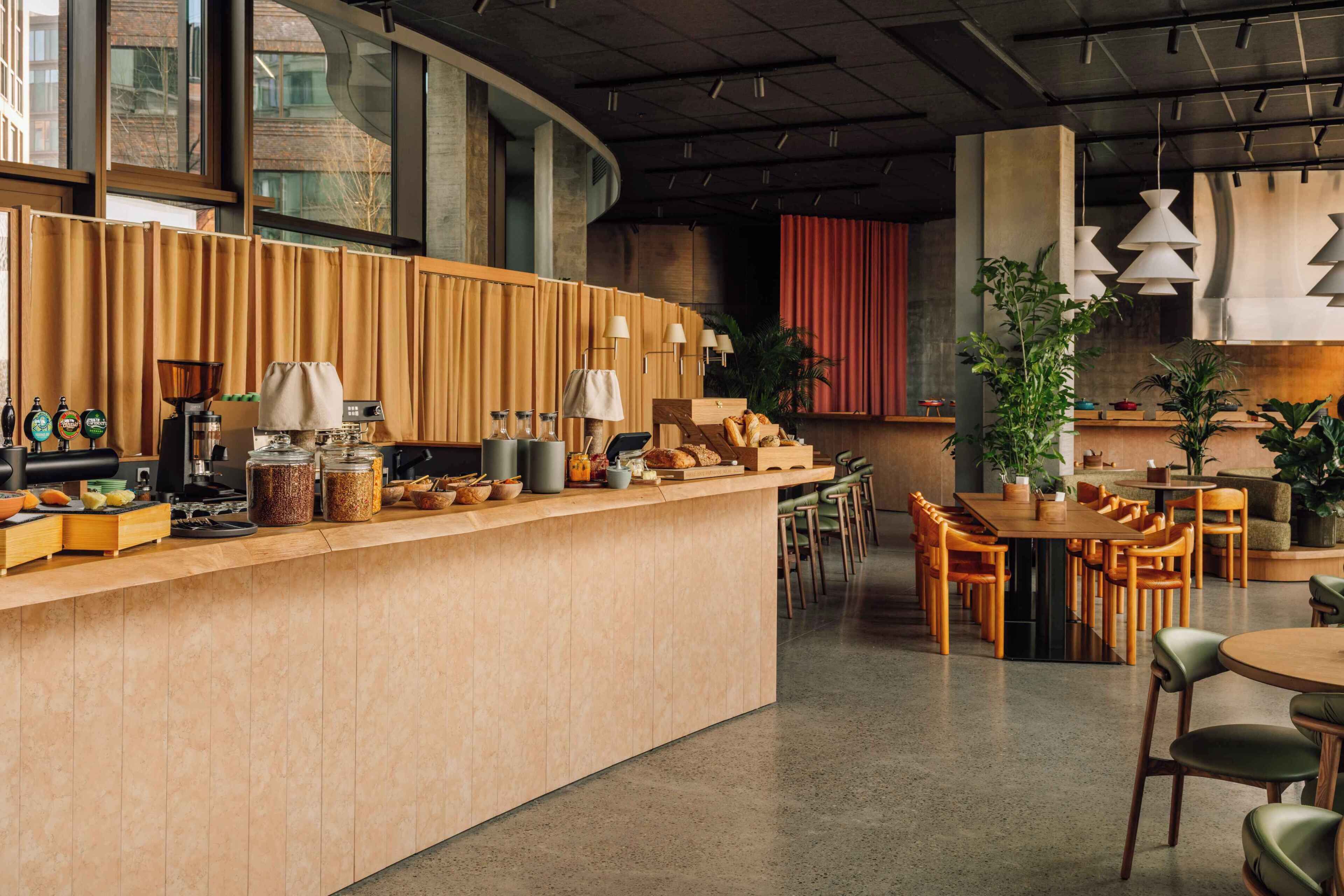Un café moderno con una barra larga, zona de asientos y grandes ventanales.