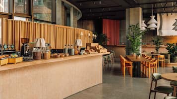 Un café moderno con una barra larga, zona de asientos y grandes ventanales.