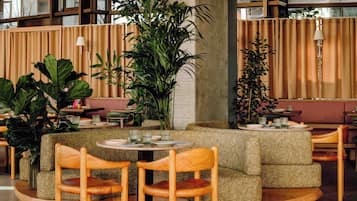A cozy seating area with cushioned sofas and wooden chairs, surrounded by large potted plants and a round table with a tray of items.