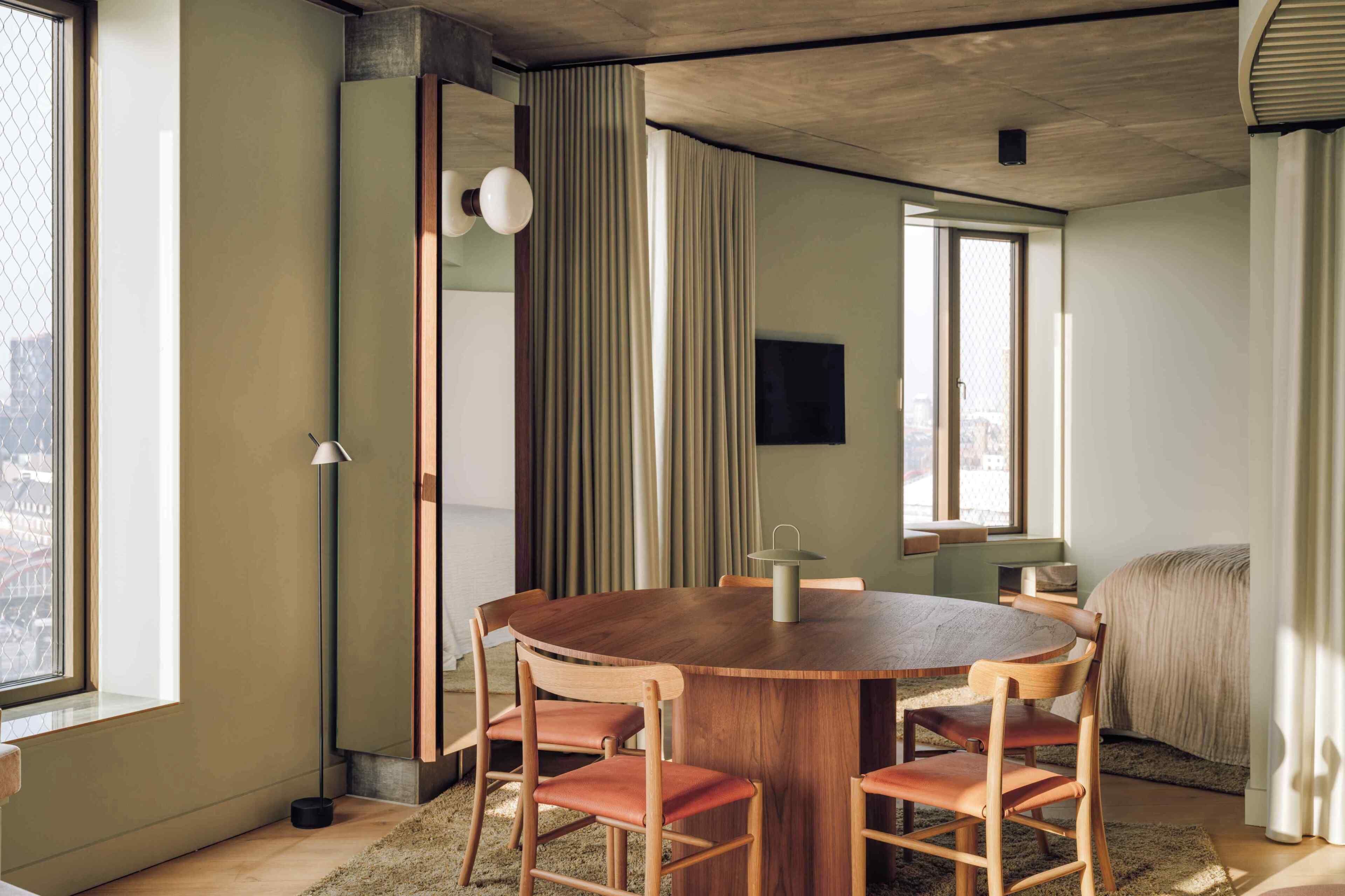 A round wooden table with four chairs, a floor lamp, and a window with curtains.