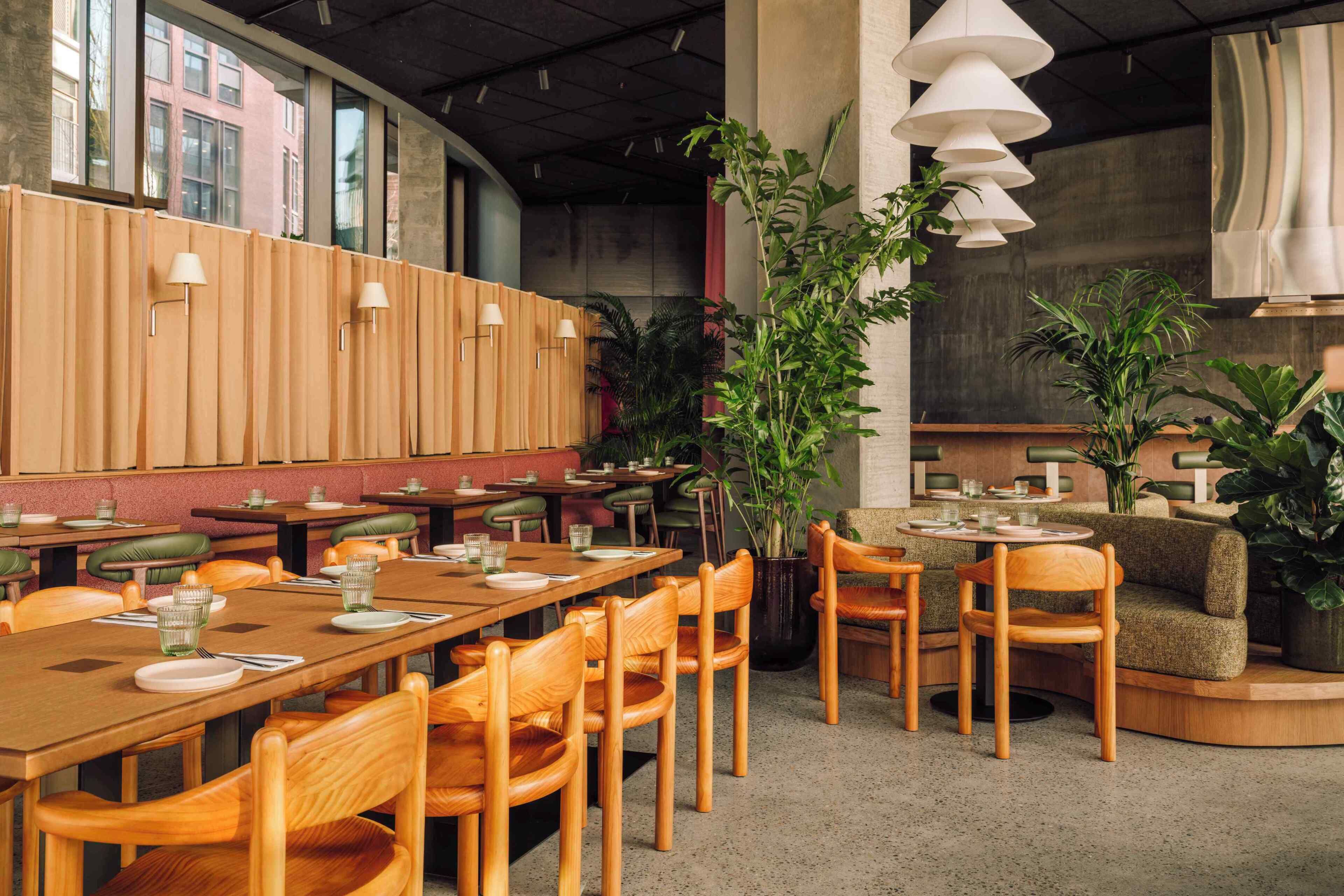 A restaurant with wooden tables and chairs, potted plants, and pendant lighting.