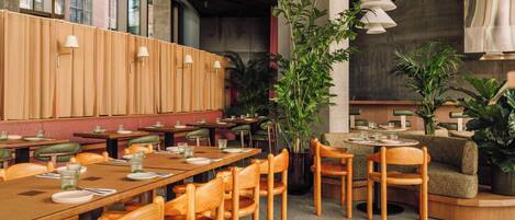 A restaurant with wooden tables and chairs, potted plants, and pendant lighting.