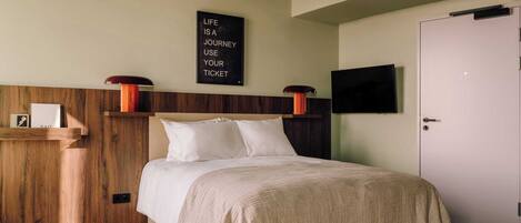 A bedroom with a bed, a mounted TV, a wooden headboard, a wall-mounted shelf, and a motivational quote.