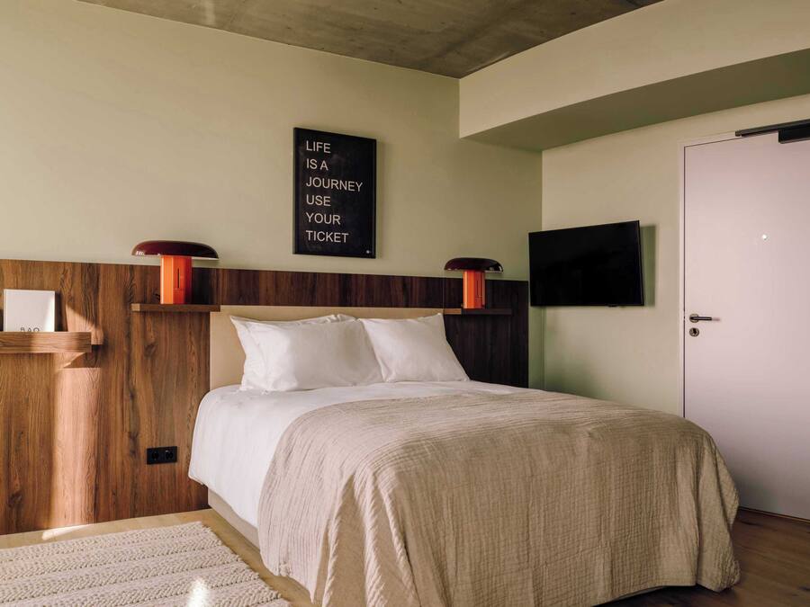 Un dormitorio con cama, televisor montado, cabecero de madera, estante en la pared y una cita motivacional.