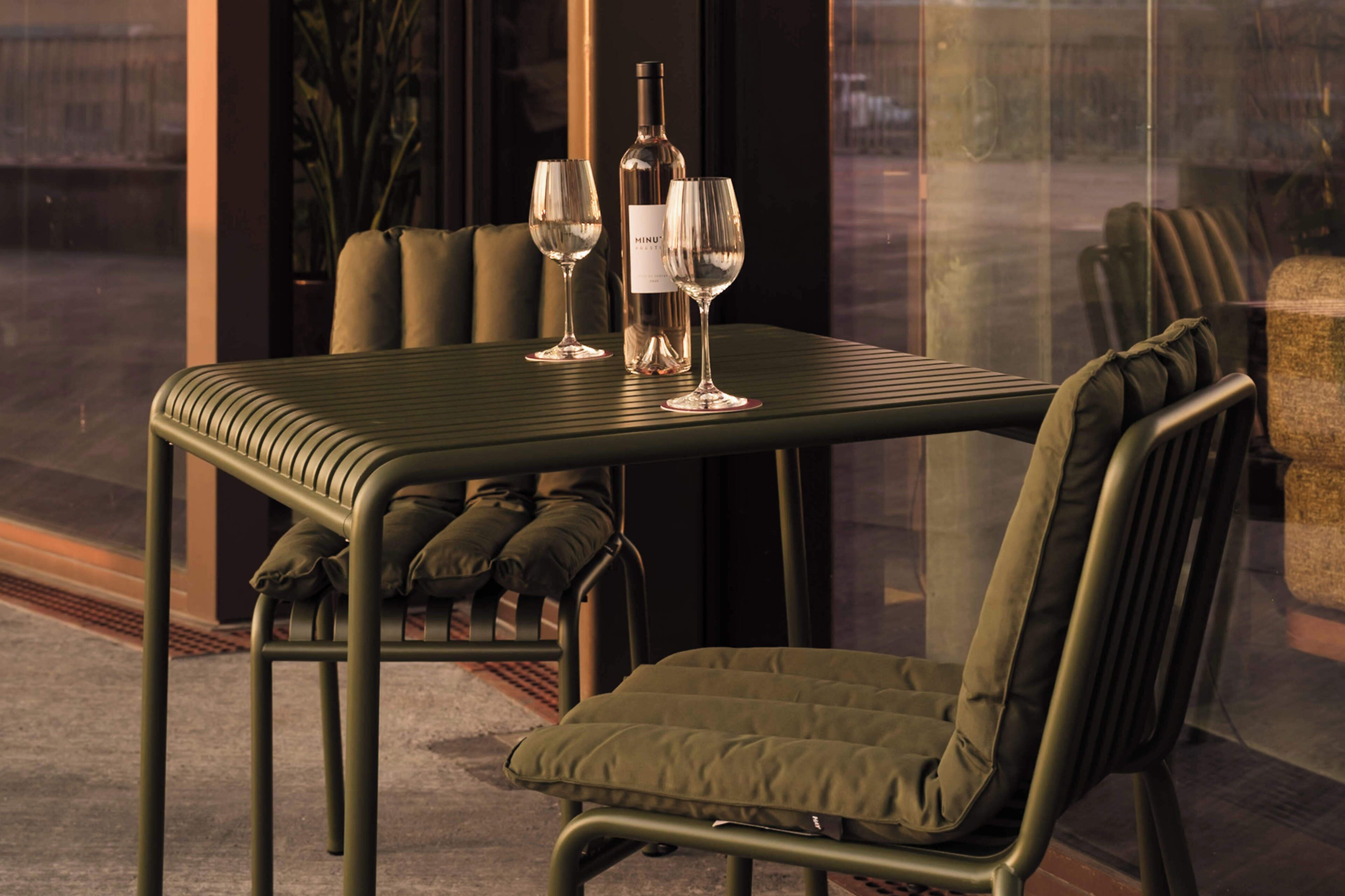 A table with two wine glasses and a bottle, set against a window with a view.