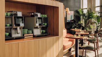 Una estación de café moderna con máquinas de espresso y un área de estar con mesas y sillas.