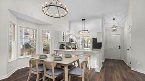 A modern kitchen with white cabinets, a central island, and a dining area with a wooden table and chairs. - NEW Fully Remodeled Home w/ Office Workspace, Patio, 3 Bed, 2 Bath (Holly Springs)