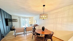Un vaste espace de vie comprenant une table et des chaises en bois rond, un canapé et une grande fenêtre agrémentée de rideaux.