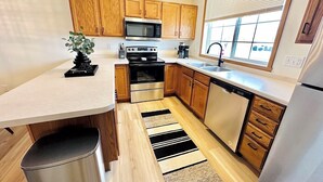 Une cuisine moderne avec des meubles en bois, des appareils électroménagers en acier inoxydable, un tapis à rayures noires et blanches et une fenêtre avec des stores.