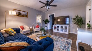 A living room with a blue sofa, a glass coffee table, and a ceiling fan. - Hamilton Hideaway  (Fortville)