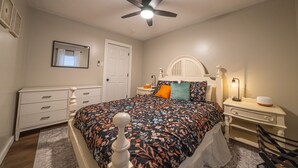 A bedroom with a bed, a nightstand, a dresser, a ceiling fan, and a door. - Hamilton Hideaway  (Fortville)