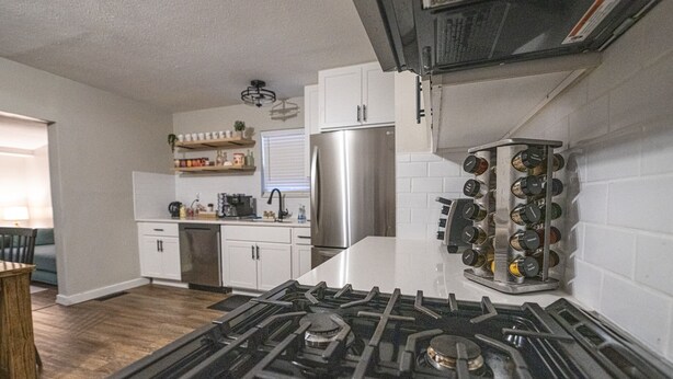 A modern kitchen with white cabinets, a stainless steel refrigerator, a gas stove, and a spice rack. - Hamilton Hideaway  (Fortville)